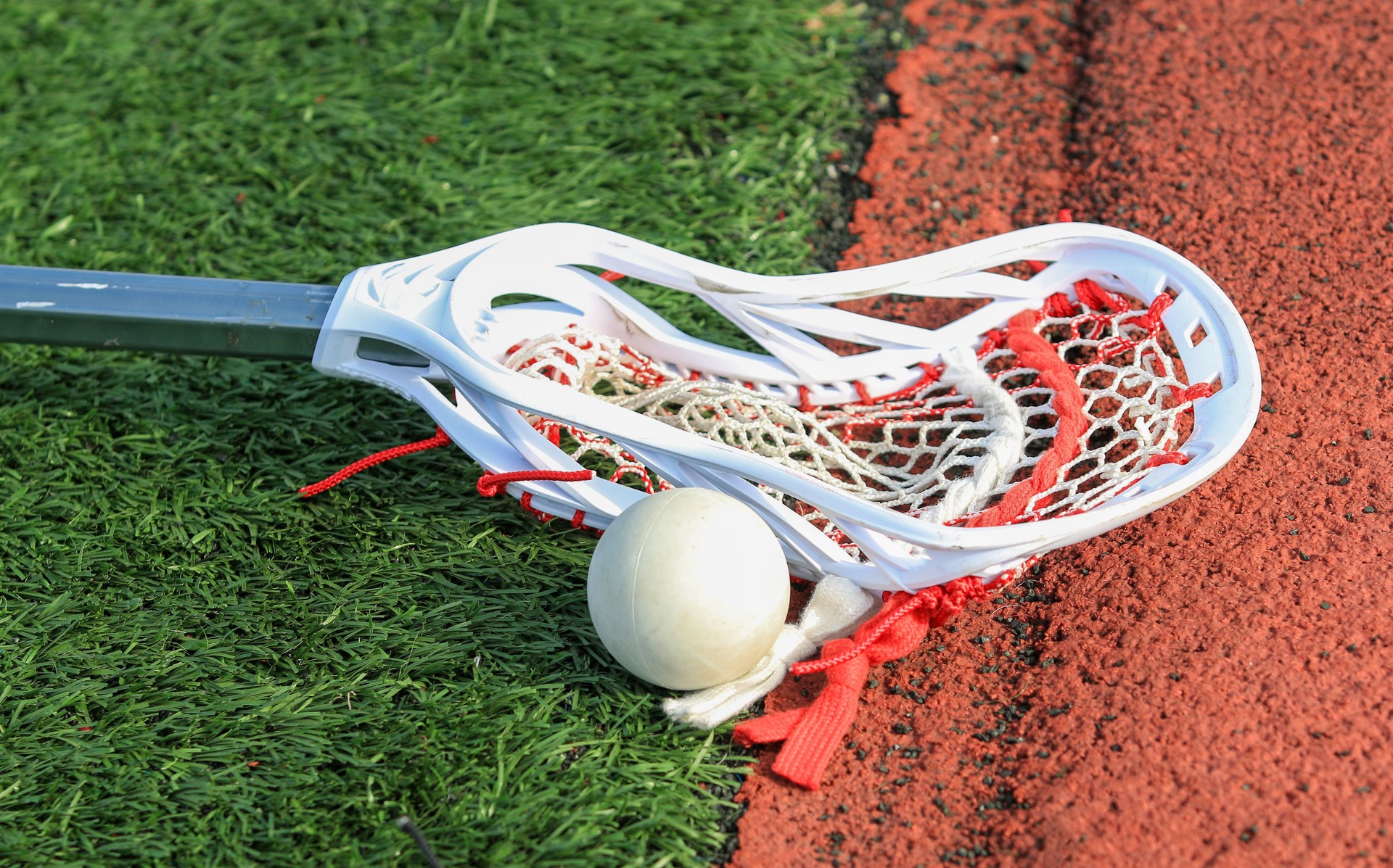 Lacrosse Stick and Ball on Artificial Turf Near a Track at a Sports Facility